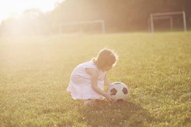 Küçük kız gün batımında sahada top oynuyor..