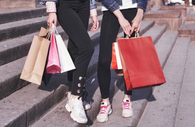 Two young woman carrying shopping bags while walking in the street after visiting the stores.