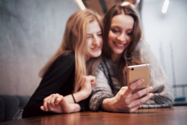 Teke tek toplantı. Kafede masada oturan iki genç iş kadını. Kız arkadaş imajı smartphone ekranda gösterir. Masada kapalı bir dizüstü bilgisayardır. Toplantı arkadaşlar.