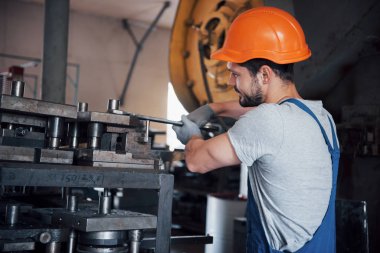 Büyük bir metal fabrikasında kasketli genç bir işçinin portresi. Makinelere hizmet eden mühendis, gaz ekipmanları için parça üretiyor..