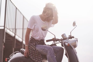 Güzel bir hippi kızın portresi siyah bir scooter 'da oturuyor, gülümsüyor poz veriyor ve ılık bahar güneşinin tadını çıkarıyor..