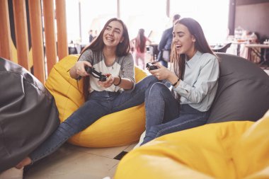 İkiz kız kardeşler konsolda oynarlar. Kızlar joystickleri ellerinde tutup eğleniyorlar..