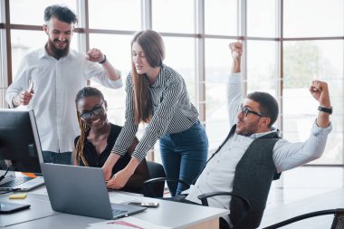 Genç çalışanlar masadaki ofiste oturuyor ve bir dizüstü bilgisayar kullanıyorlar, bir ekip beyin fırtınası konsepti üzerinde çalışıyor.