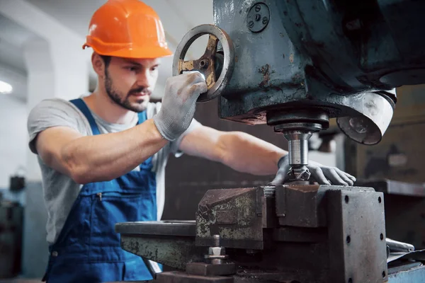Büyük bir metal fabrikasında kasketli genç bir işçinin portresi. Makinelere hizmet eden mühendis, gaz ekipmanları için parça üretiyor..