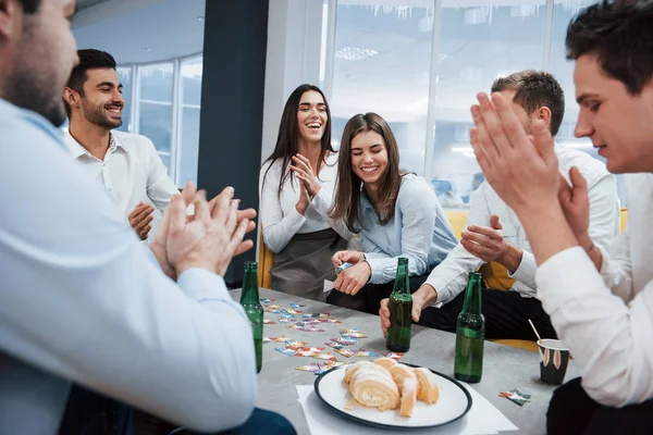 Everyone is smiling. Celebrating successful deal. Young office workers sitting near the table with alcohol.