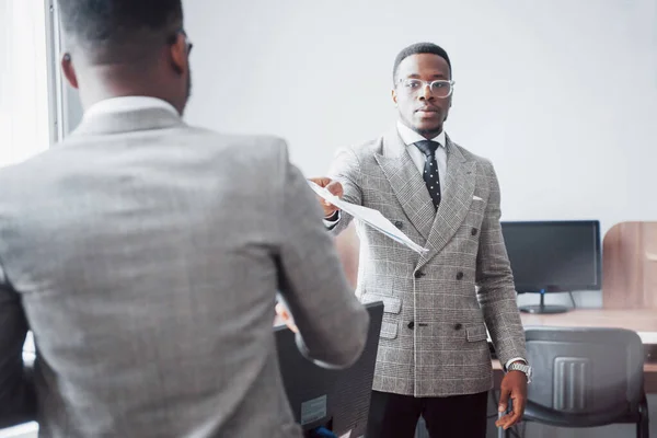 Discussing a project. Two black business people in formalwear discussing something while one of them pointing a paper.