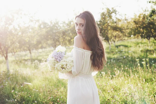 白い光のドレスを着た美しい少女と夏の花の花束は庭で素晴らしい一日を過ごします — ストック写真