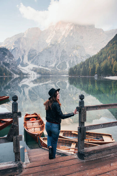 Great distance. Fog on the top of the hills. Woman in black hat enjoying majestic mountain landscape near the lake with boats.