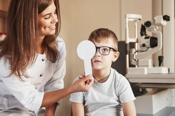 Skoncentrowany Chłopiec Kobieta Lekarz Obejmuje Dziecko Oko Narzędziem Medycznym Sprawdzania — Zdjęcie stockowe