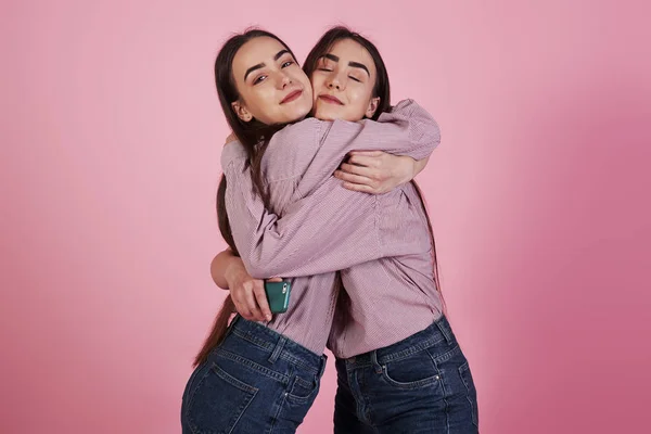 在粉红背景的演播室里 两个穿着相同衣服的姐姐拥抱在一起 — 图库照片