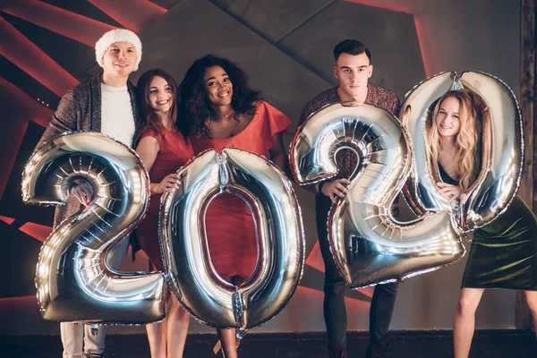 Wishing well. Group of beautiful young friends with inflatable numbers in hands celebrating new 2020 year.