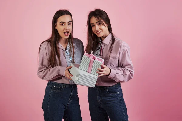 送给你节日礼物 在粉红背景的演播室里玩乐的年轻女人可爱的双胞胎 — 图库照片