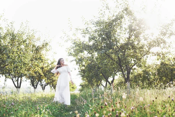 一个穿着白色长裙的小女孩正在花园里散步 美丽的落日穿过树叶 — 图库照片