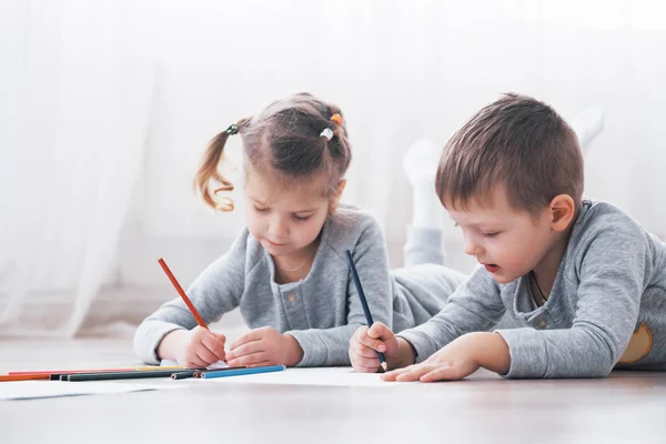 Children lie on the floor in pajamas and draw with pencils. Cute child painting by pencils.