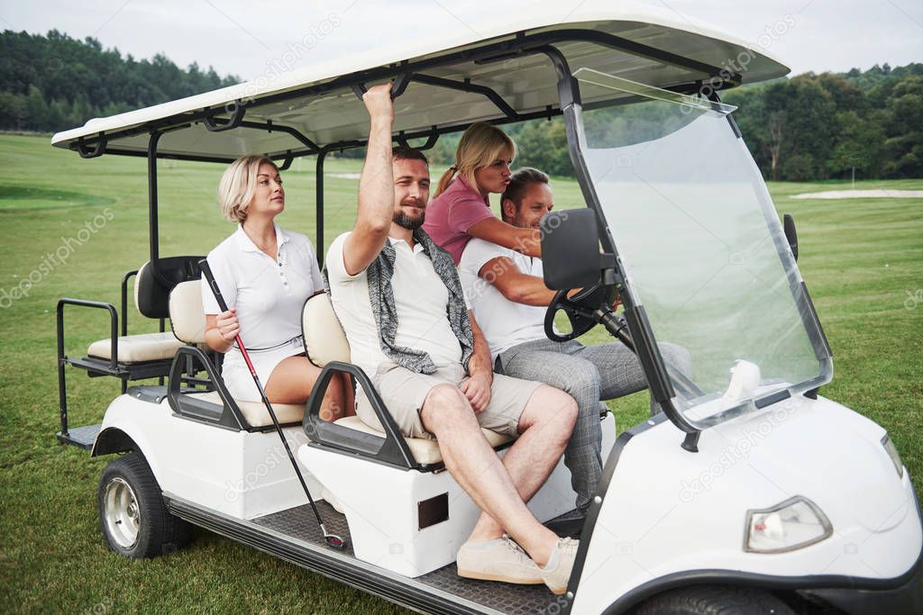Young couples getting ready to play. A group of smiling friends came to the hole on a golf cart.
