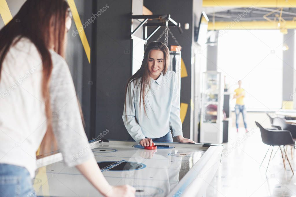 Two beautiful twin girls play air hockey in the game roomand have fun.