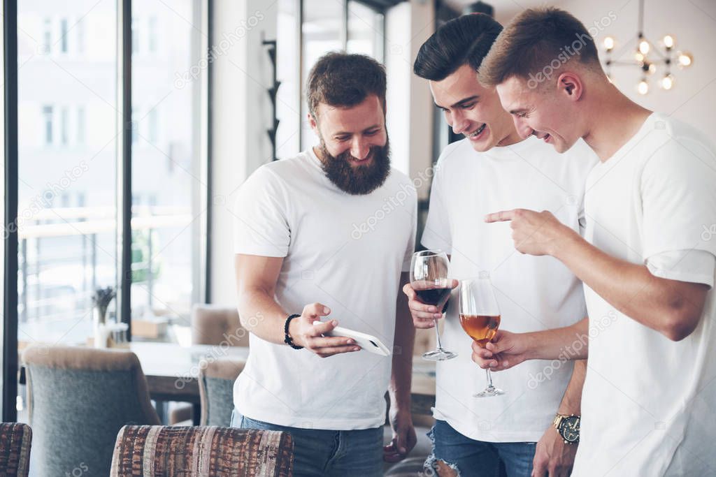 Cheerful old friends communicate with each other and phone watch, with glasses of whiskey or wine in pub. Concept of entertainment and lifestyle. Wifi connected people in bar table meeting.