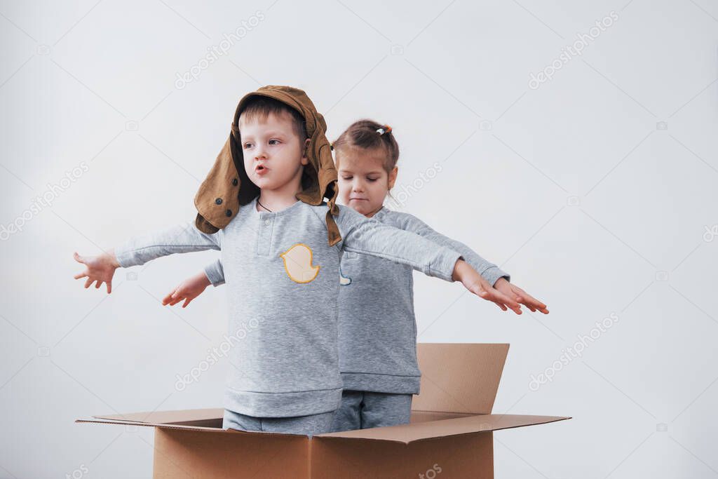 Playful childhood. Little boy having fun with cardboard box. Boy pretending to be pilot. Little boy and girl having fun at home.