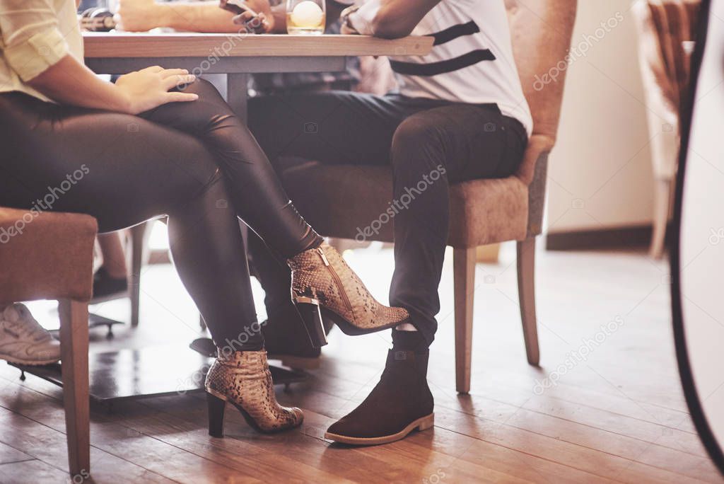 Girl flirting with a guy touching leg her foot under the table in a cafe while having fun with the friends. Flirt with your foot during lunch.