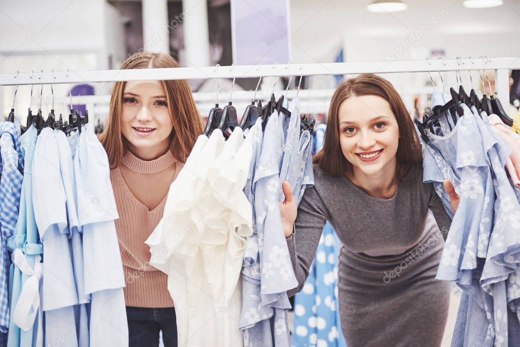 The best friends together spend time. Two beautiful girls make purchases in the clothing store. They dressed in the same clothes.