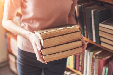 Eski kütüphanenin kitap raflarının yanında edebiyat arayan genç bir kız.,