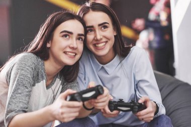 İkiz kız kardeşler konsolda oynarlar. Kızlar joystickleri ellerinde tutup eğleniyorlar..