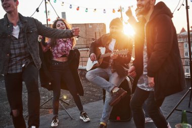 Güneşli bir günde çatıda akustik gitar çalıp şarkı söylüyor..