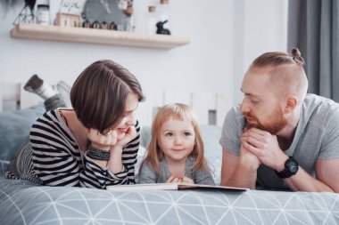 Baba, Anne ve Küçük Kız Oturma Odasında Çocuk Kitabı Okuyorlar. Mutlu büyük aile bayram gününde ilginç bir kitap okudu. Ebeveynler çocuklarını sever..