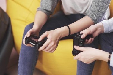İkiz kız kardeşler konsolda oynarlar. Kızlar joystickleri ellerinde tutup eğleniyorlar..