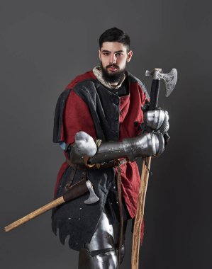 Gri arka planda ortaçağ şövalyesi. Zincirli zırhlı, kırmızı, siyah elbiseli ve savaş baltalı zalim, kirli yüzlü bir savaşçı portresi..