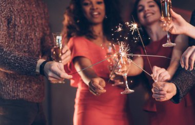 Çapraz çubuklar. Çok ırklı arkadaşlar yeni yılı kutluyor. Bengal ışıkları ve bardaklarla içki içiyorlar..