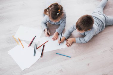 Çocuklar pijamalarıyla yere yatar ve kalemle çizerler. Kalemlerle resim yapan şirin bir çocuk..