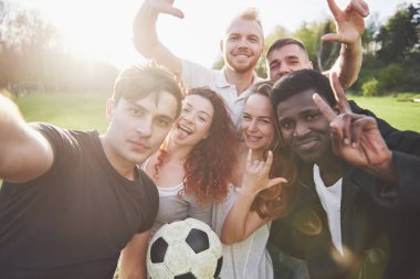 Gündelik kıyafetli bir grup arkadaş futbol sahasında sefi yapıyor. İnsanlar eğleniyor ve eğleniyor. Aktif dinlenme ve manzaralı gün batımı.