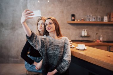 İki kız gülümsüyor ve bir kafede akıllı telefon kullanıyor..