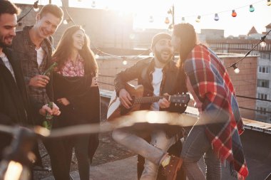 Benimle şarkı söylemeye devam et. Güneşli sonbahar gününde alkollü ve akustik gitarlı çatı partisi.