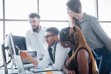 Genç çalışanlar masadaki ofiste oturuyor ve bir dizüstü bilgisayar kullanıyorlar, bir ekip beyin fırtınası konsepti üzerinde çalışıyor.