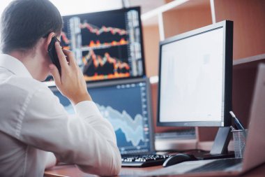 Telefondan sipariş alırken borsacıların online alım-satımları sayesinde. Arka planda dosya ve veri analizleriyle dolu çoklu bilgisayar ekranları.