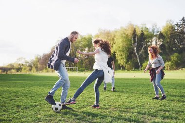 Gündelik kıyafetli bir grup arkadaş açık havada futbol oynuyor. İnsanlar eğleniyor ve eğleniyor. Aktif dinlenme ve manzaralı gün batımı.