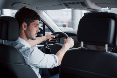 Genç bir adam yeni alınmış bir arabada oturuyor ve ellerini dümene koyuyor.