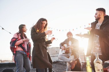 Harika güneş ışığı. Alkol içen ve gitar çalan bir çatı partisi. Arkasında güneş ışığı.