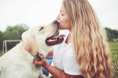 Parkta yeşil çimlerin üzerinde güzel bir köpeği olan güzel bir kızı çerçevelet.