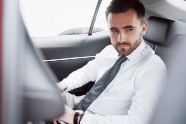 Genç bir işadamı, arabasının arkasında otururken işlerini not defteriyle ayarlıyor..