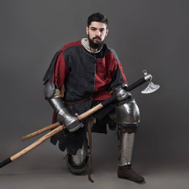 Gri arka planda ortaçağ şövalyesi. Zincirli zırhlı, kırmızı, siyah elbiseli ve savaş baltalı zalim, kirli yüzlü bir savaşçı portresi..