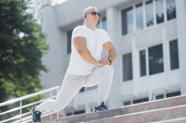 Spor kıyafetli yakışıklı bir fitness adamı, modern şehirde ciddi egzersizlere hazırlanırken esneme hareketleri yapıyor..