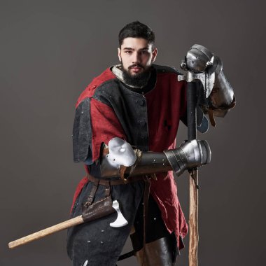 Gri arka planda ortaçağ şövalyesi. Zincirli zırhlı, kırmızı, siyah elbiseli ve savaş baltalı zalim, kirli yüzlü bir savaşçı portresi..
