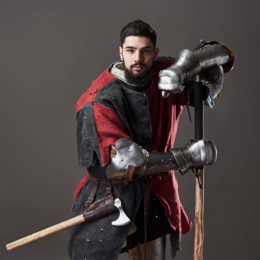 Gri arka planda ortaçağ şövalyesi. Zincirli zırhlı, kırmızı, siyah elbiseli ve savaş baltalı zalim, kirli yüzlü bir savaşçı portresi..