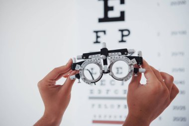Phoropter in the picture. Woman hands holding the glasses on background of the eye chart. clipart