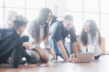 Modern ofisteki genç yaratıcı insanlar. Bir grup genç iş adamı dizüstü bilgisayarla birlikte çalışıyor. Serbest çalışanlar yerde oturuyor. İşbirliği kurumsal başarı. Takım çalışması konsepti.