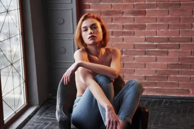 Muhteşem bir kadın doğrudan kameraya bakıyor. Kız sandalyeye oturur. Yarı çıplak çekici genç bir kadın seksi vücudunu gösteriyor..