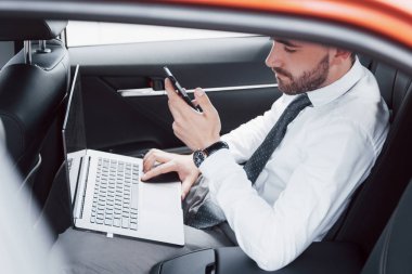 Genç bir iş adamı dizüstü bilgisayarda çalışıyor ve arabanın arkasında otururken telefonla konuşuyor. Hareket halinde çalışır, zamanını takdir eder..